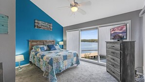 Un dormitorio con cama, cómoda, ventilador de techo, ventana con vista a un lago, y un cartel en la pared.
