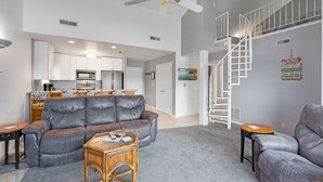 Una sala de estar moderna con un sofá gris, una mesa de centro de madera y una escalera que conduce a un nivel superior.