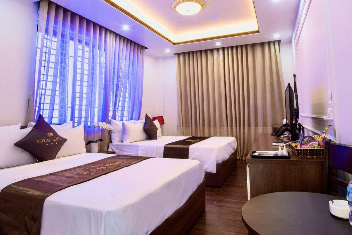 Ein Hotelzimmer mit zwei Betten, einem Schreibtisch, einem Stuhl und einem großen Fenster mit Vorhängen.