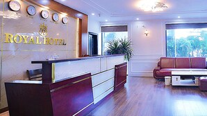 A hotel reception area with a marble counter, clocks displaying time in multiple cities, a seating area with a sofa, and a large window offering a view. - Royal Hotel II (Hanoi)