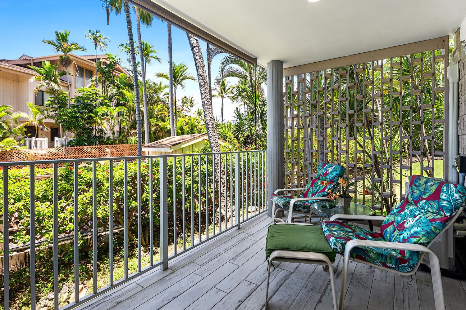 Un balcon agrémenté de deux chaises et d’une table, entouré d’une rambarde en métal et de plantes tropicales luxuriantes.