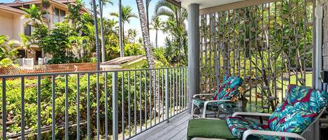 Un balcon agrémenté de deux chaises et d’une table, entouré d’une rambarde en métal et de plantes tropicales luxuriantes.