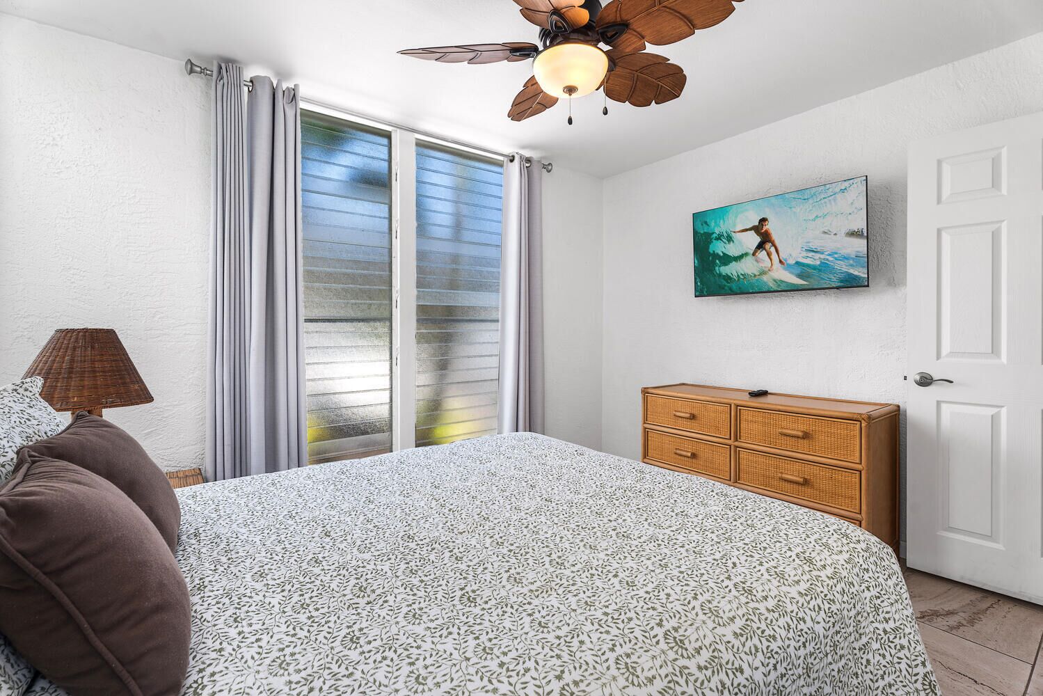 Quarto com cama, penteadeira, ventoinha no teto, pintura e janela com cortinas.