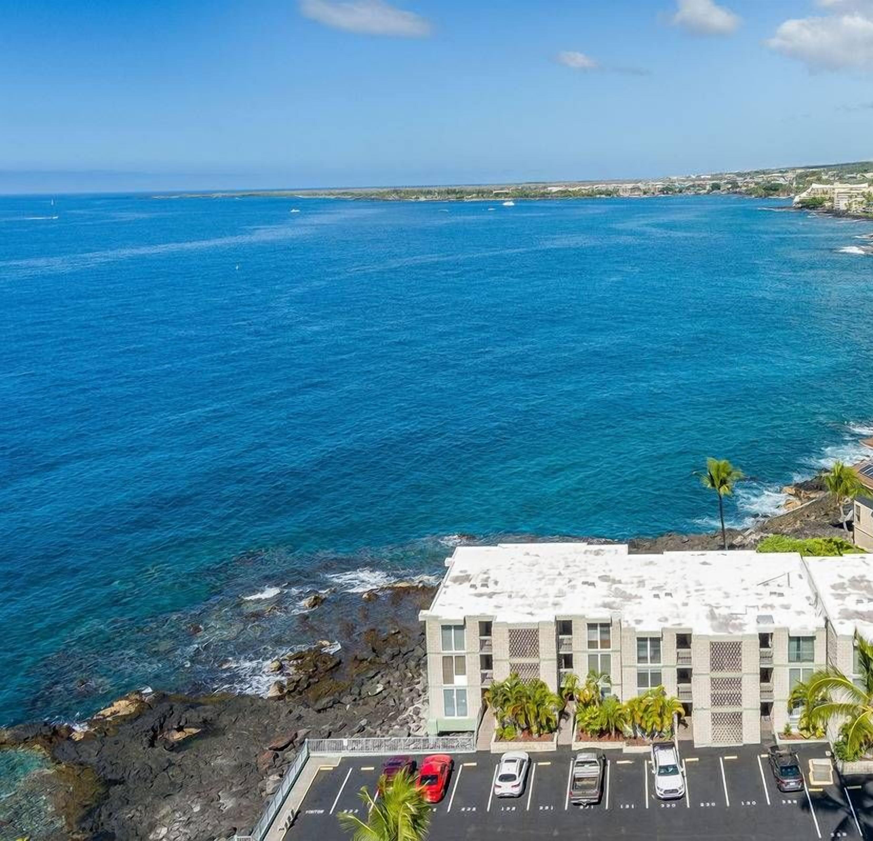 A coastal hotel with a view of the ocean, parking, and solar panels.