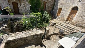 Un edificio de piedra con un pequeño jardín, una parrilla y una silla de descanso blanca.