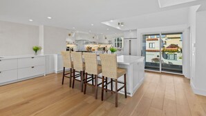 A modern kitchen with white cabinetry, a central island with bar stools, and a view of the outside through a sliding glass door.