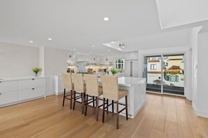 Una cocina moderna con armarios blancos, una isla central con taburetes altos y vistas al exterior a través de un ventanal corredero.