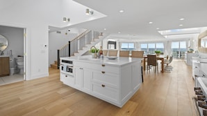 A spacious kitchen with a large island, wooden flooring, and a staircase leading to an upper level.