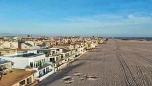 A coastal residential area with houses along a sandy beach, featuring a clear sky and a visible moon.