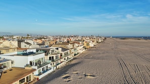 Zona residencial costera con casas a lo largo de una playa arenosa, con cielo despejado y luna visible.