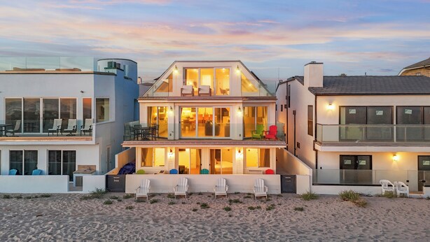 A beachfront property with a two-story house featuring balconies, outdoor seating, and a beach view.