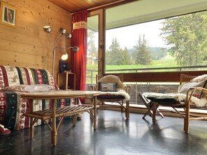 Una habitació acollidora amb interior de fusta, una finestra gran amb vista a vegetació, una taula i dues cadires.