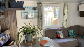 Een moderne woonkamer met een bank, een eettafel, een plant in pot en een raam met gordijnen.