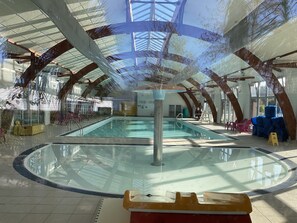 An indoor swimming pool with a glass floor, surrounded by wooden beams and glass walls, offering a view of the sky and trees. - Mobil Home (Gastes)