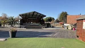 Een overdekt buitengebied met een podium, zitplaatsen en een houten terras.