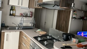 Een moderne keuken met houten kastjes, een roestvrijstalen spoelbak, een gasfornuis en een televisie waarop een programma wordt vertoond.