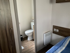 A small, clean bathroom with a toilet, a white radiator, and a wooden headboard. - Mobil Home (Gastes)