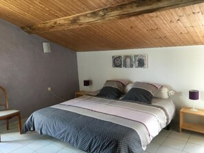 Ein Schlafzimmer mit Holzboden, einem Bett mit gemusterten Textilien, zwei Nachttischen mit Lampen und einem Sessel.