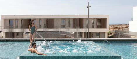 A modern hotel with a swimming pool, a spa area, and a view of the beach.