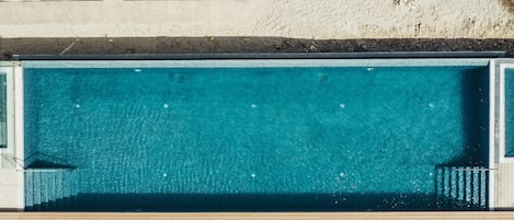 Una piscina rectangular con agua azul cristalina, rodeada por una terraza de madera con sillas de descanso.