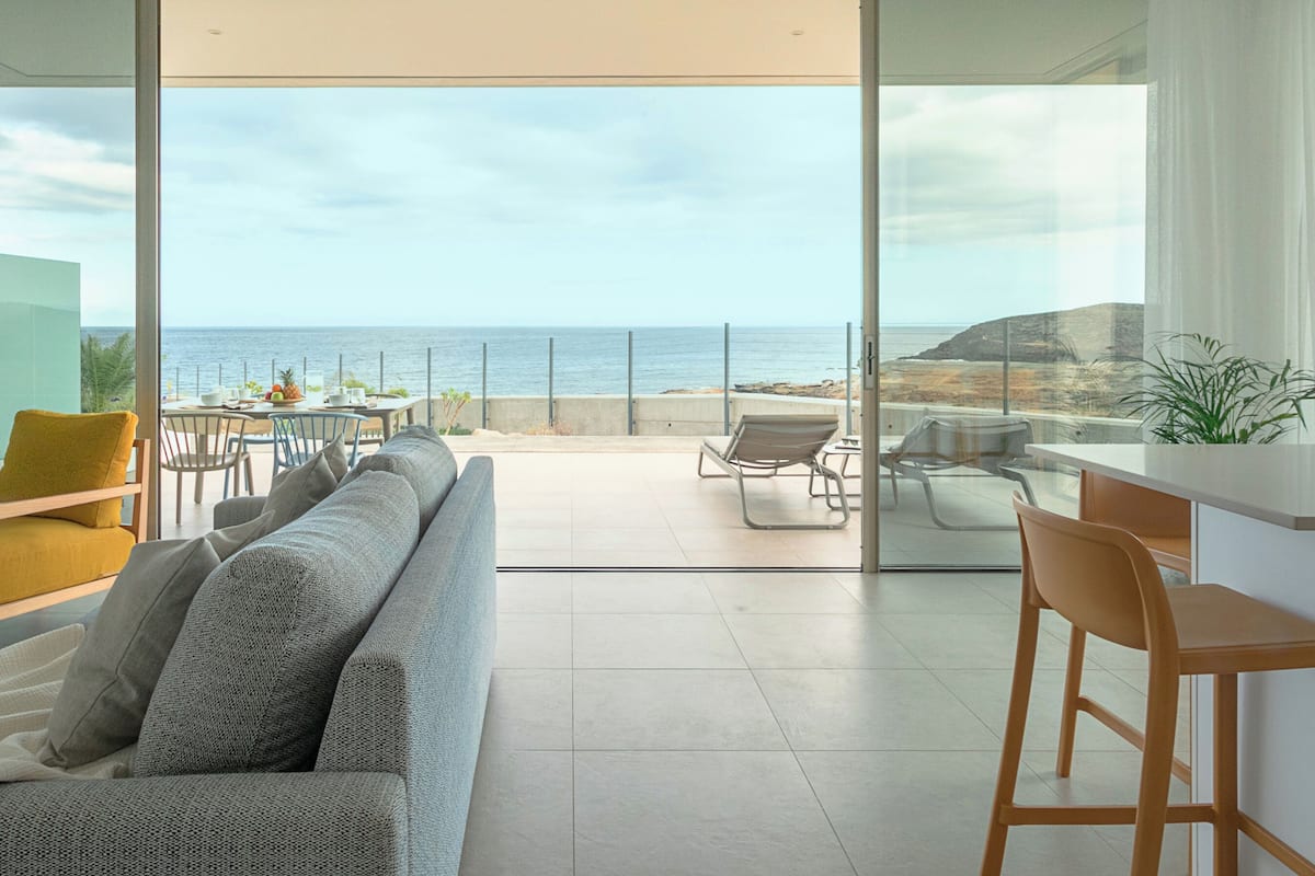 Una sala de estar moderna con un amplio ventanal que da a un balcón con vistas al mar.