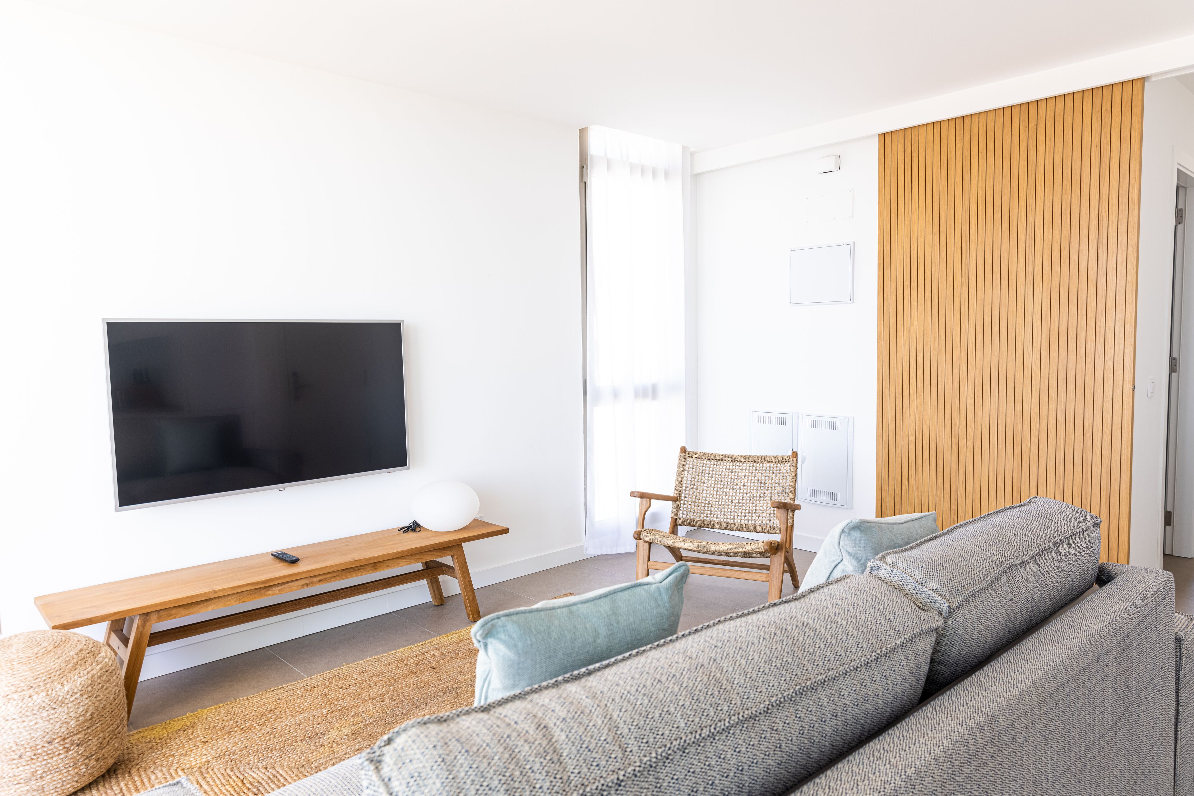 A modern living room with a flat-screen TV, wooden furniture, and a large window.