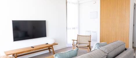 A modern living room with a flat-screen TV, wooden furniture, and a large window.