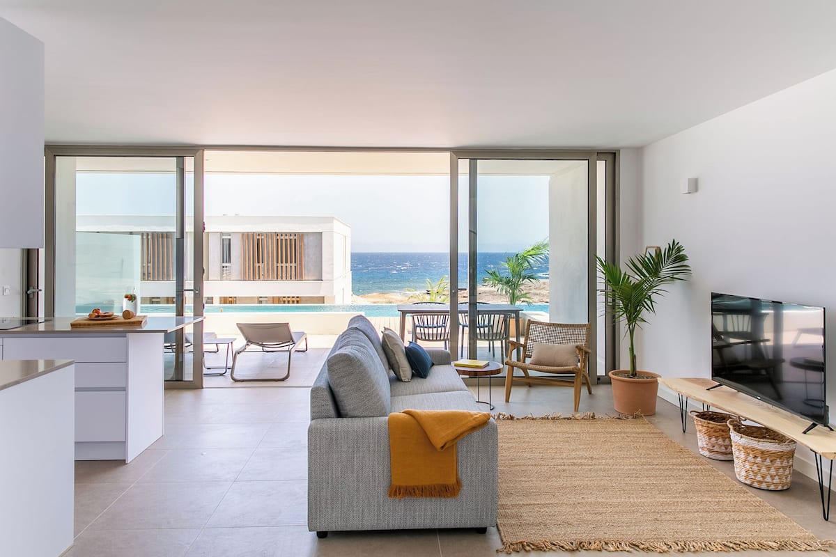 Una sala de estar moderna con un sofá, televisor y vista al océano.