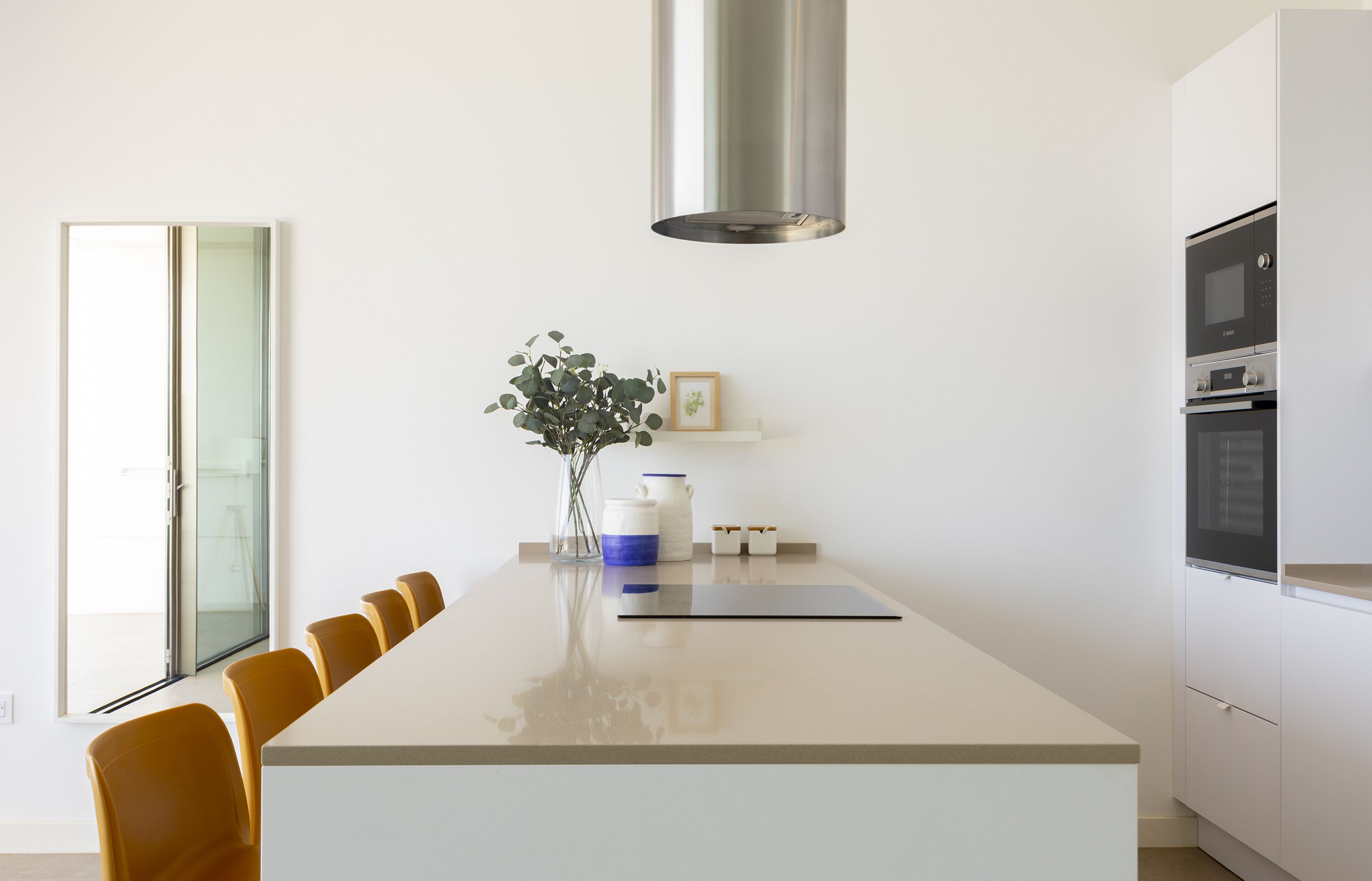 Une cuisine moderne dotée d’un îlot central, de meubles blancs et d’une hotte de cuisine en acier inoxydable.