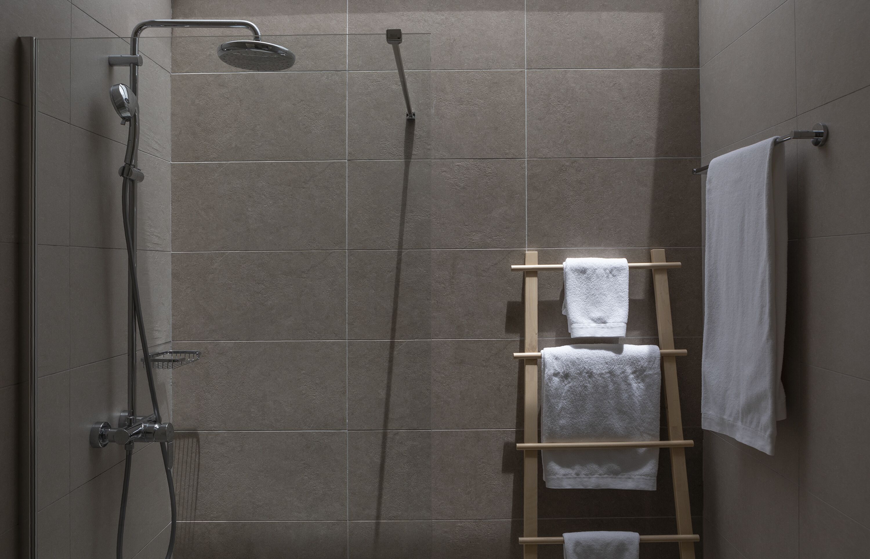 Un espace douche doté d’une porte en verre, d’un porte-serviettes en bois et d’une serviette accrochée au mur.