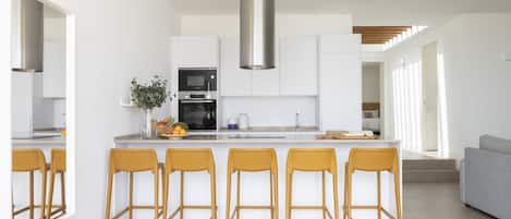 A modern kitchen with white cabinets, a stainless steel range hood, and a central island with bar stools.