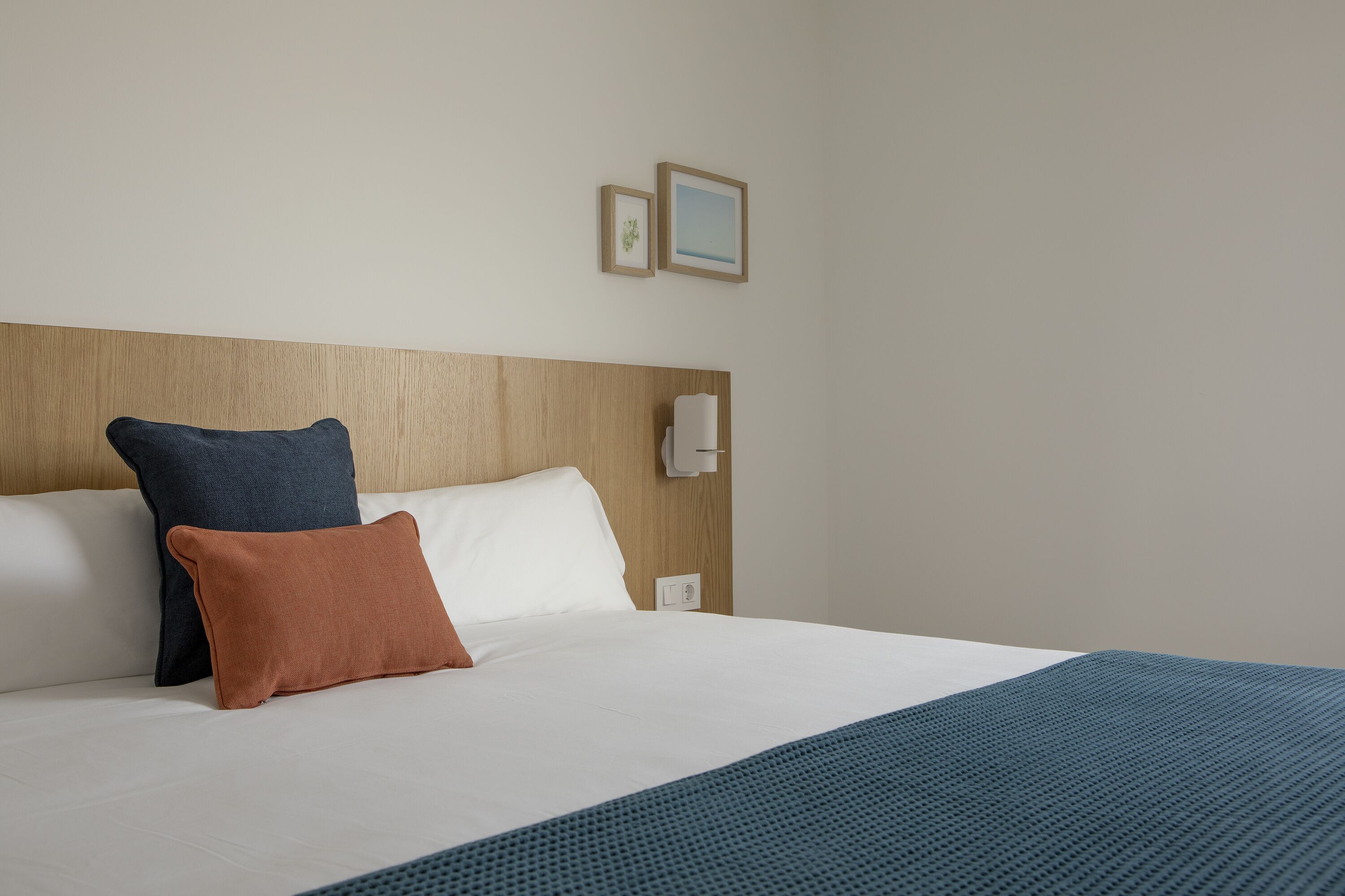 Un letto rifatto con lenzuola bianche, due cuscini, una coperta blu e una testiera in legno.