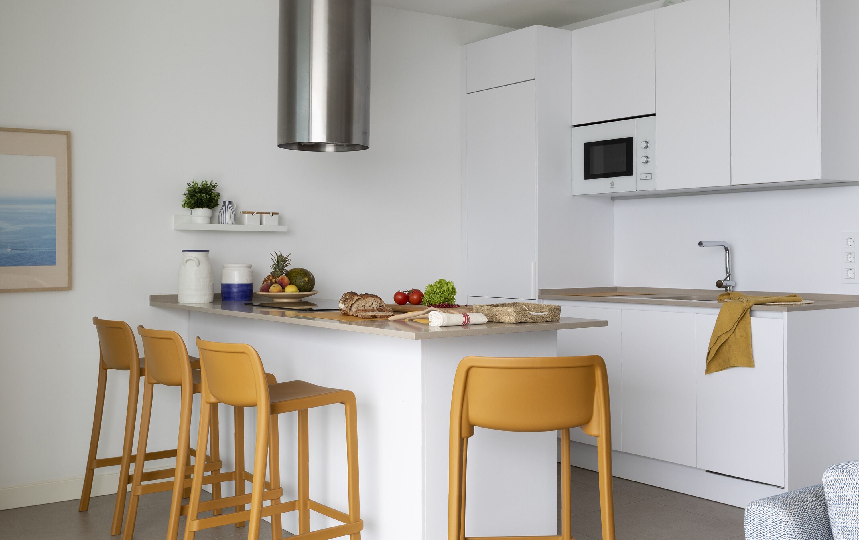 A modern kitchen with white cabinets, a stainless steel range hood, a microwave, and a bar area with stools.