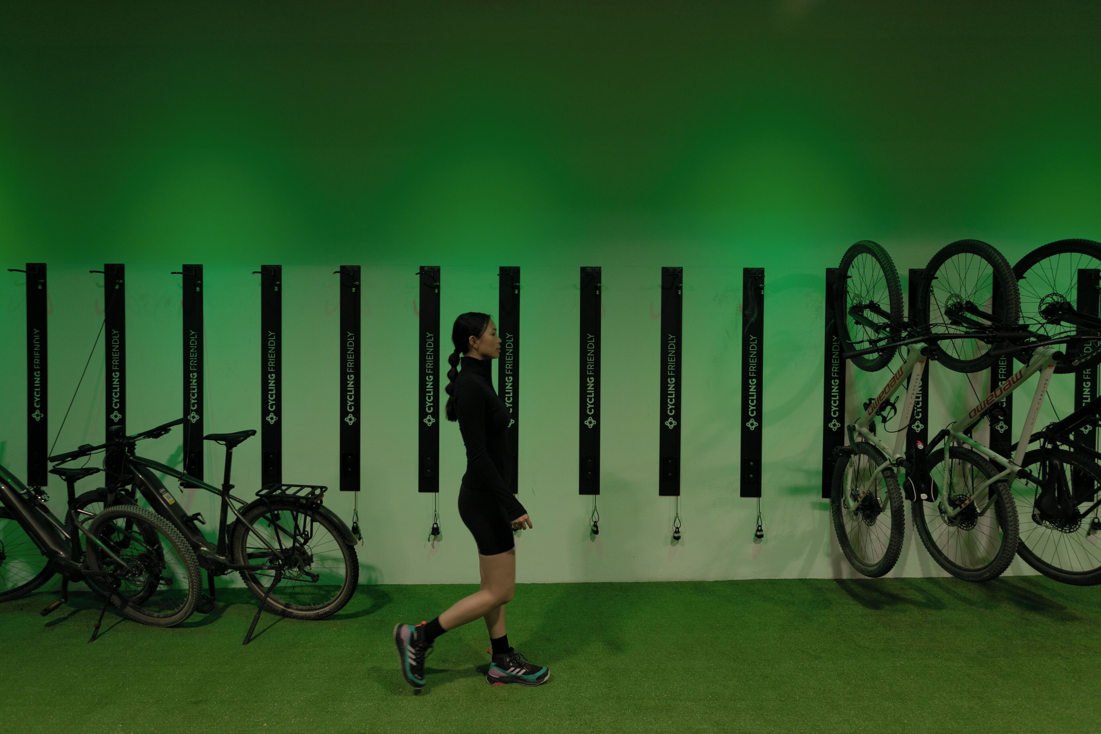 A person walking past a wall with multiple bicycles and a green background.