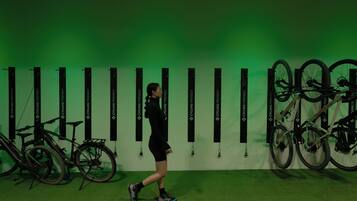 Una persona caminando cerca de una pared con varias bicicletas y un fondo verde.