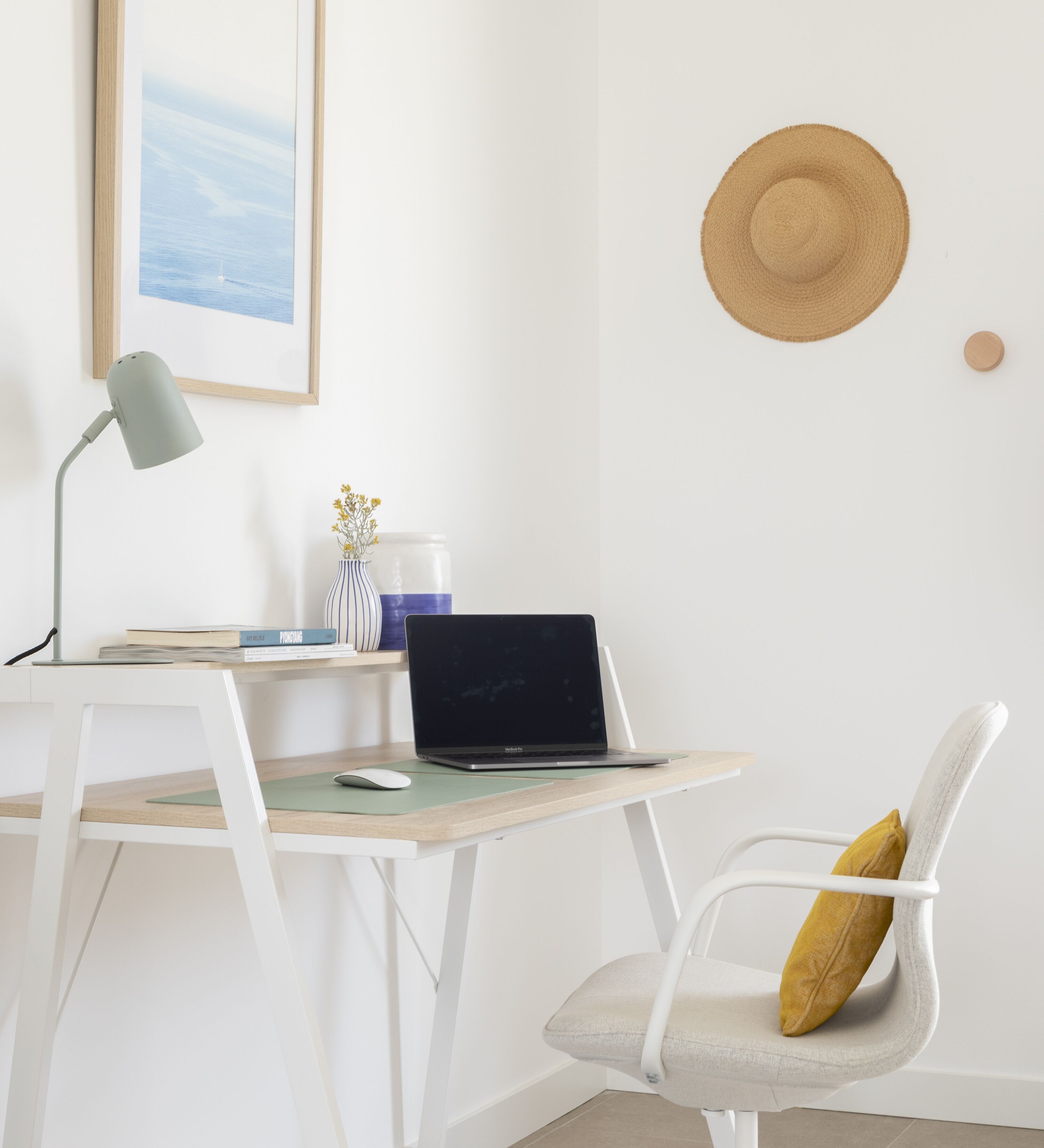 A minimalist workspace with a laptop, a desk lamp, a chair, and a framed picture on the wall.