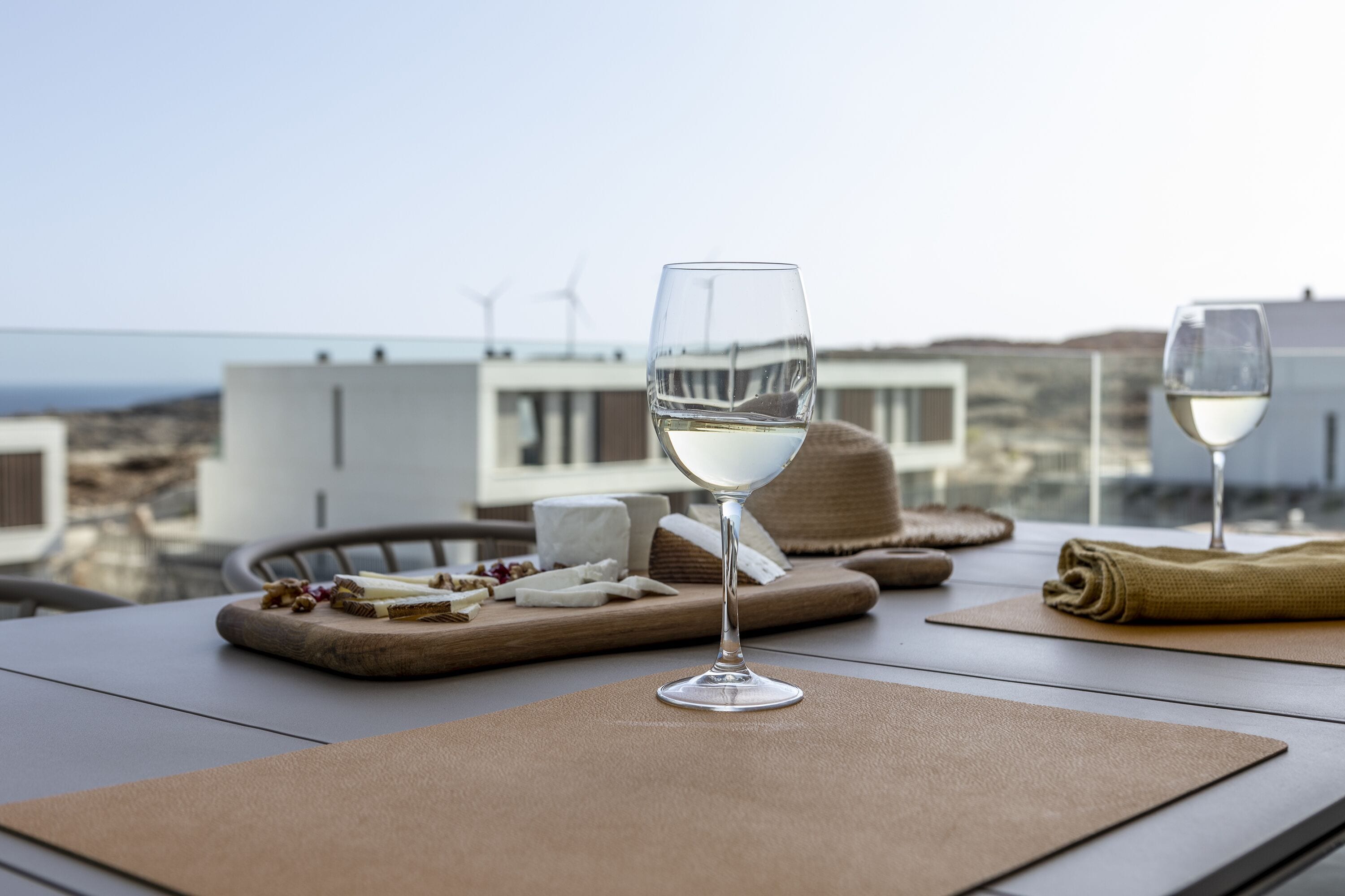 Una mesa con una copa de vino blanco, una tabla de madera con queso y uvas, y una servilleta.