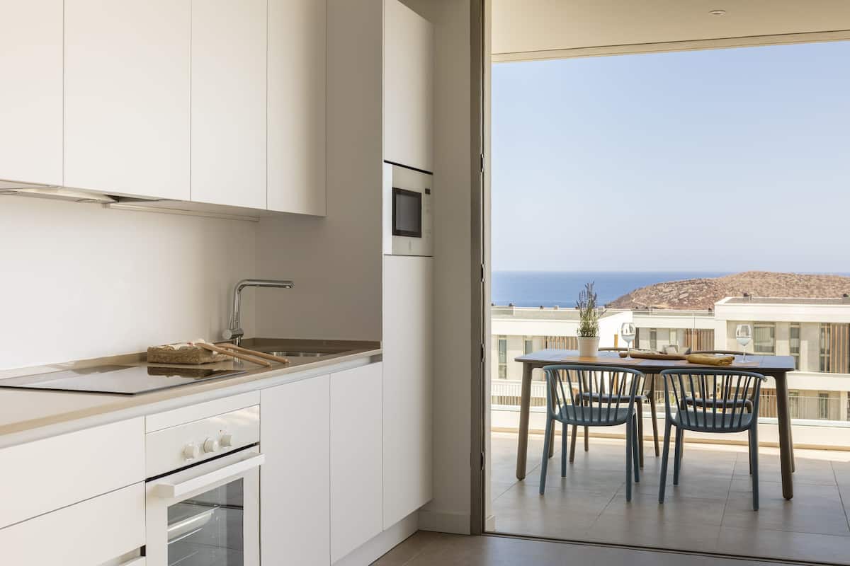 Una cocina moderna con armarios blancos, un microondas integrado y vistas al mar a través de un ventanal.