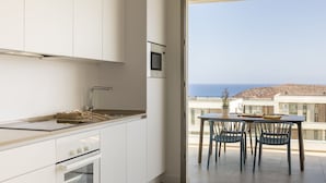 A modern kitchen with white cabinets, a built-in microwave, and a view of the sea through a glass door. - Kora Nivaria Beach (Arico)