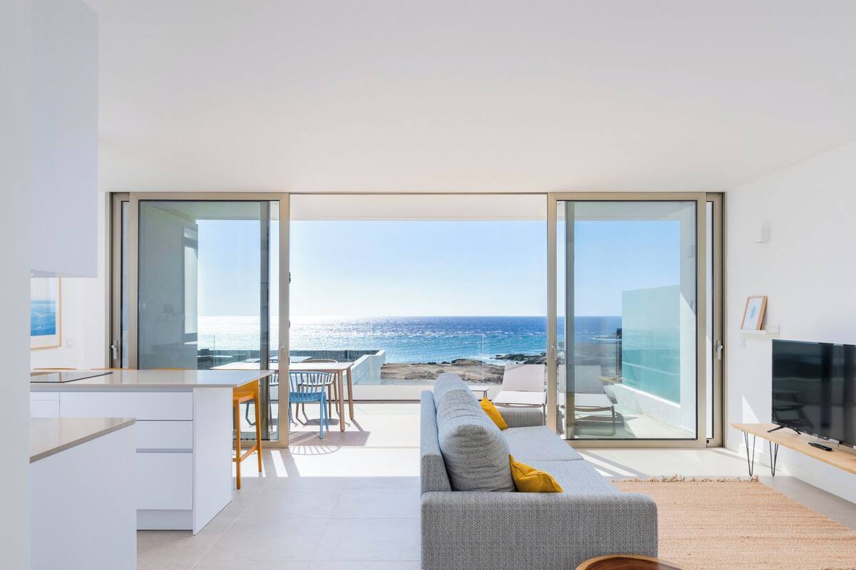 Un salón moderno con un amplio ventanal corredero que da a un balcón con vistas al mar.