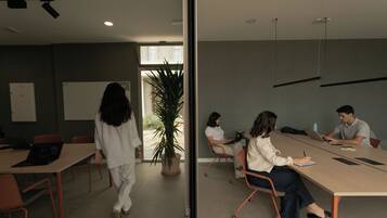 Un salón de conferencias con una larga mesa, sillas, una pizarra y una planta en maceta.