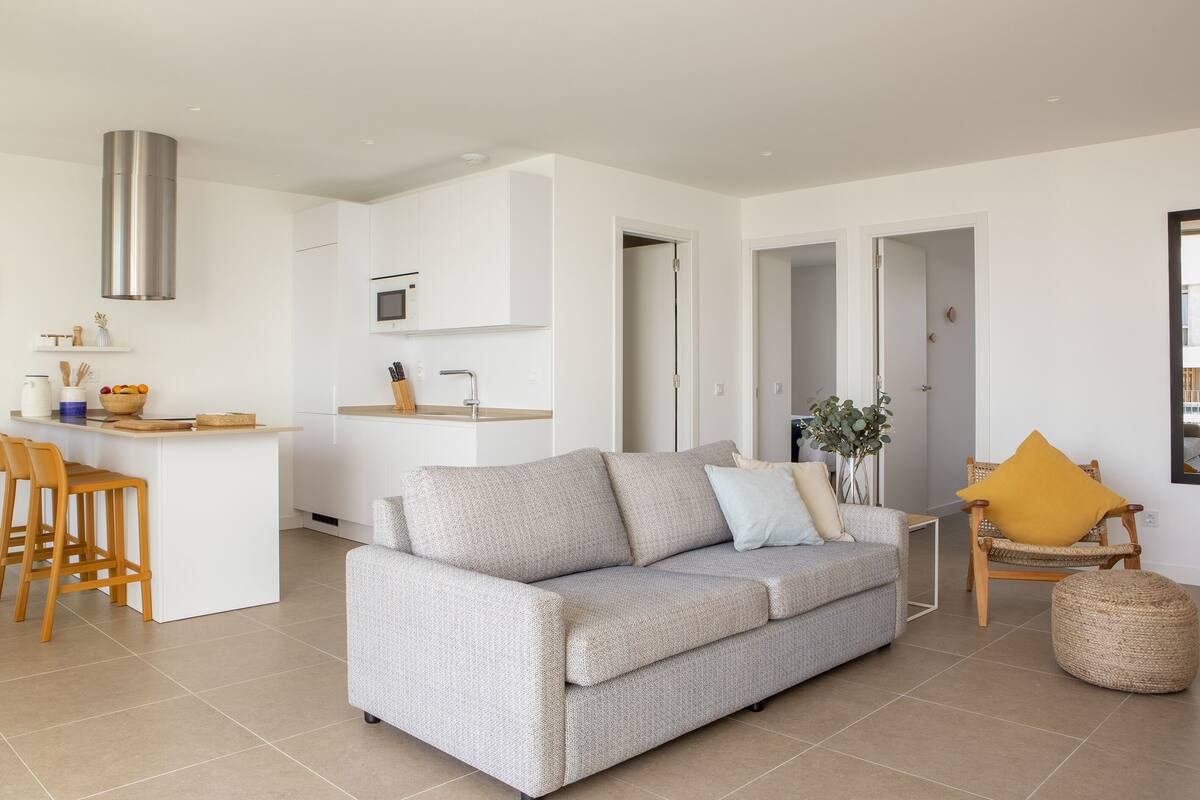 Un espacio habitable moderno con sofá, comedor con sillas, cocina con microondas y un amplio ventanal.