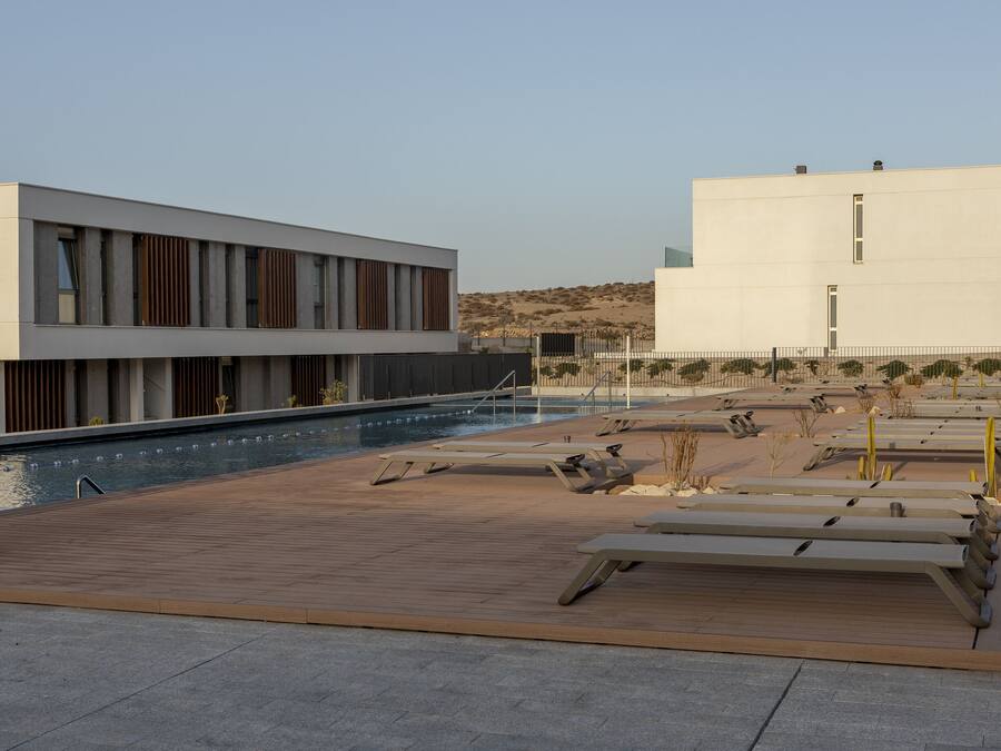 Un edificio moderno con zona de piscina, que incluye tumbonas y una terraza de madera.