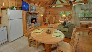 L’intérieur chaleureux d’un chalet avec une cheminée en pierre, des meubles en bois et un téléviseur fixé au mur.