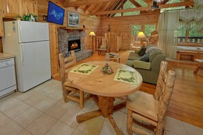 A cozy cabin interior with a stone fireplace, wooden furniture, and a television mounted on the wall.
