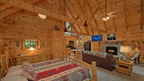 Interior de una cabaña de troncos con cama, chimenea, televisión y muebles de madera.