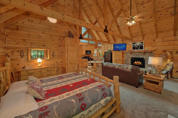 A log cabin interior with a bed, fireplace, television, and wooden furniture.