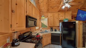 Cocina rústica de cabaña con estufa, microondas, refrigerador y armarios de madera.