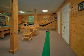 A wooden cabin interior with a pool table, chairs, a hammock, and a billiards table.