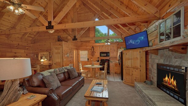Un interior de cabaña acogedor con techo de madera, chimenea, televisor, sofá y una mesa de comedor.